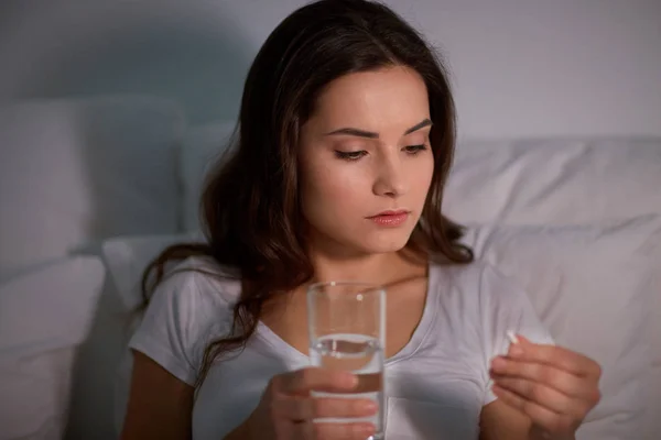 Mujer con píldora y vaso de agua en la cama en casa — Foto de Stock