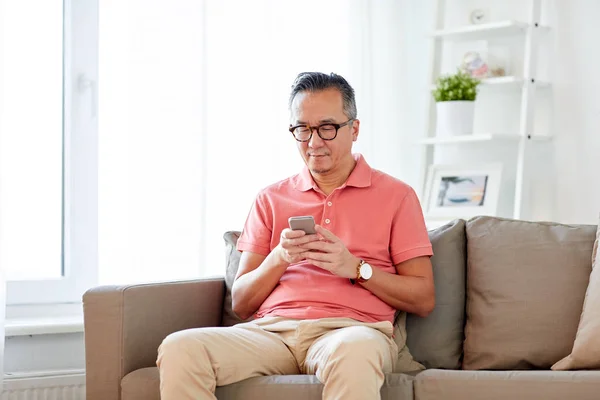 Hombre con teléfono inteligente sentado en el sofá en casa — Foto de Stock