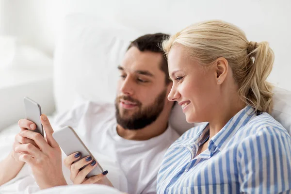 Gelukkige paar met smartphones in bed thuis — Stockfoto