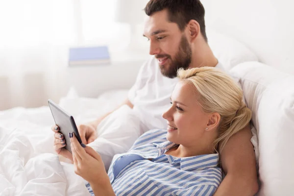 Sorridente coppia felice con tablet pc a letto a casa — Foto Stock