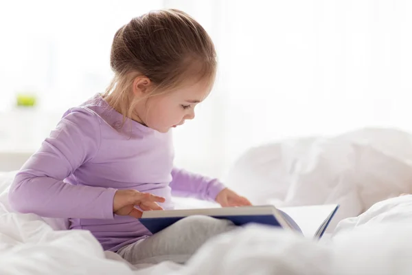 Heureuse petite fille lecture livre dans le lit à la maison — Photo