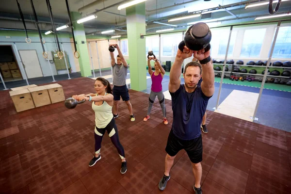 Grupo de pessoas com kettlebells se exercitando no ginásio — Fotografia de Stock