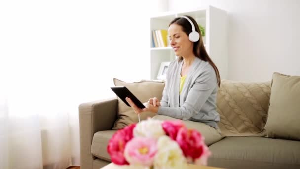 Счастливая женщина с планшетным компьютером и наушниками дома — стоковое видео