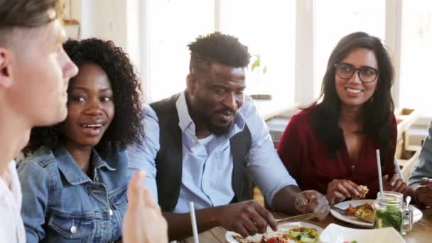 Счастливые друзья едят и разговаривают в ресторане — стоковое видео