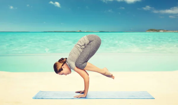 Donna che fa yoga in posa gru sul tappeto sulla spiaggia — Foto Stock