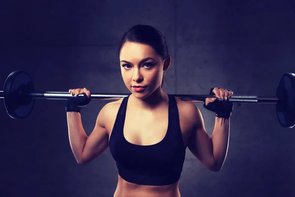 Jovem mulher flexionando músculos com barbell no ginásio — Fotografia de Stock