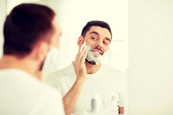 Glücklicher Mann, der Rasierschaum am Badezimmerspiegel aufträgt — Stockfoto