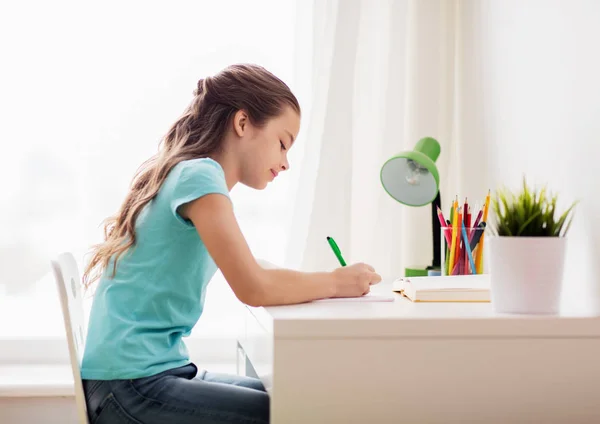 Menina feliz com livro escrevendo para notebook em casa — Fotografia de Stock