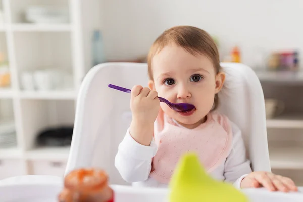 Meisje van de baby met lepel eten puree uit pot thuis — Stockfoto