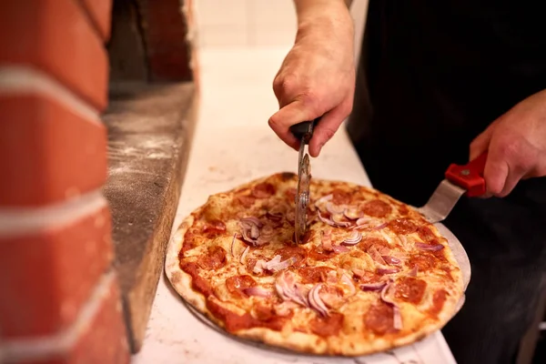 Laga händer skära pizza i bitar på pizzeria — Stockfoto