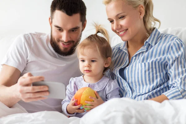 Familia feliz con teléfono inteligente en la cama en casa —  Fotos de Stock