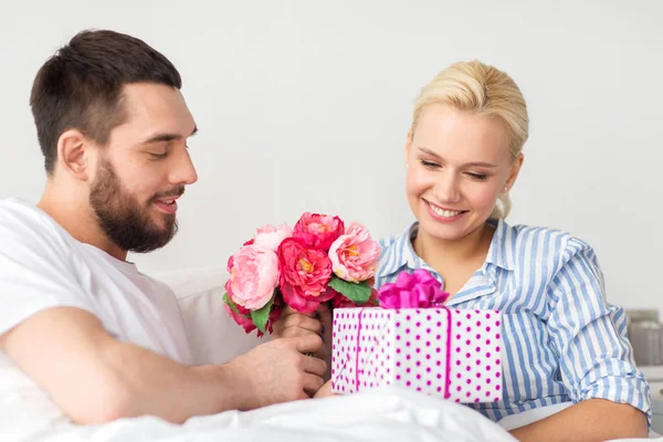 Casal feliz com caixa de presente na cama em casa — Fotografia de Stock