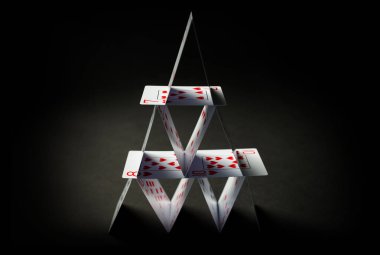house of playing cards over black background clipart