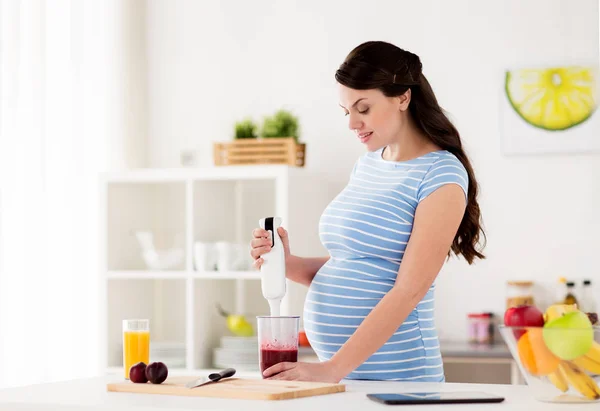 Pregnant woman with blender cooking fruits at home — Stock Photo, Image
