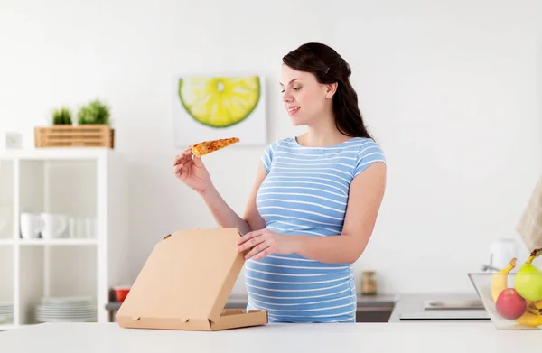 Счастливая беременная женщина ест пиццу на кухне — стоковое фото