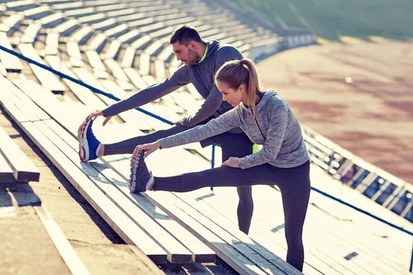 Couple stretching leg on stands of stadium — Stock Photo, Image