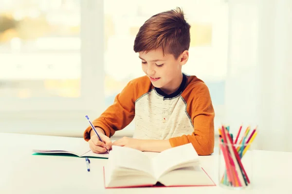 Glimlachende student jongen schrijven naar notebook thuis — Stockfoto