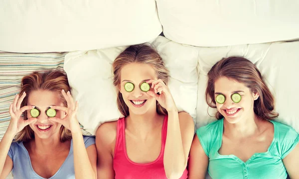 Mujeres jóvenes felices con máscara de pepino acostado en la cama — Foto de Stock