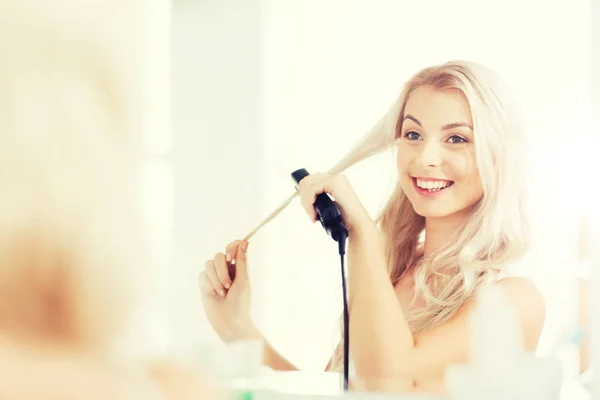 Женщина с утюгом для укладки волос в ванной комнате — стоковое фото