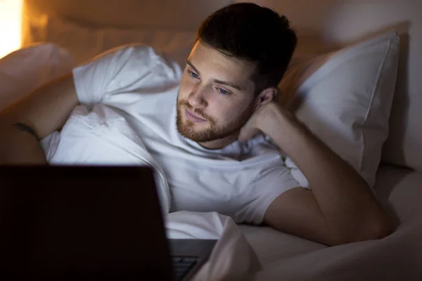 Joven con el ordenador portátil en la cama en el dormitorio en casa — Foto de Stock