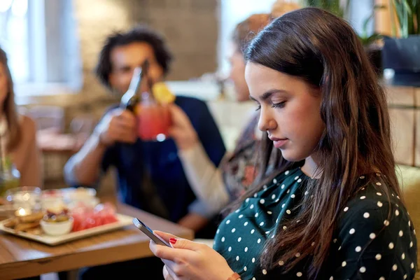 Mulher com smartphone e amigos no restaurante — Fotografia de Stock