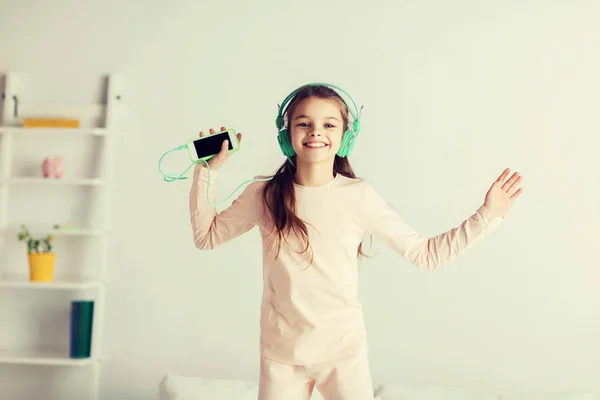 Lány jumping ágyon, smartphone és fejhallgató — Stock Fotó