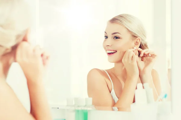 洗面所の鏡を見てイヤリングにしようとしている女性 — ストック写真