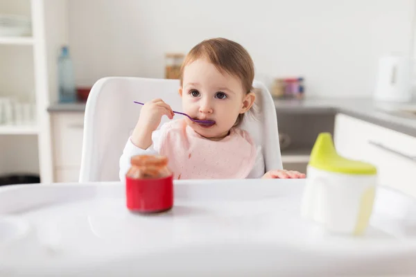 Bebê menina com colher comer purê de jar em casa — Fotografia de Stock