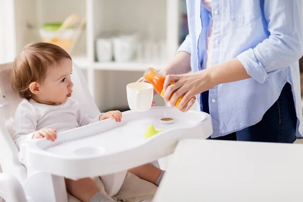 Bebê e mãe derramando suco para xícara em casa — Fotografia de Stock