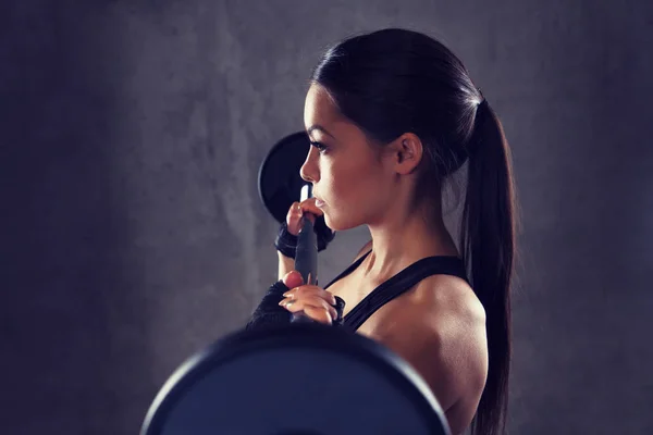 Mujer joven flexionando los músculos con barra en el gimnasio — Foto de Stock