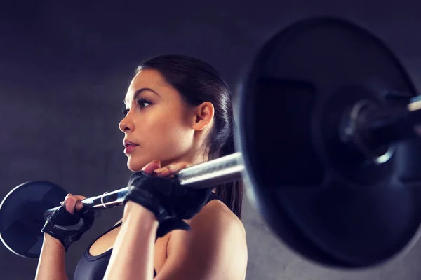Mujer joven flexionando los músculos con barra en el gimnasio — Foto de Stock