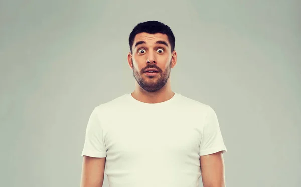 Наляканий чоловік у білій футболці на сірому фоні — стокове фото