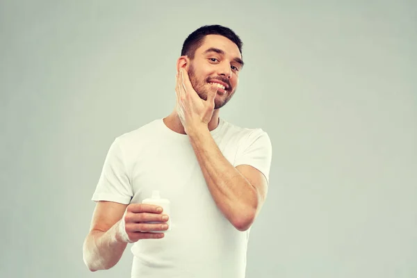 Jovem feliz aplicando creme ou loção no rosto — Fotografia de Stock