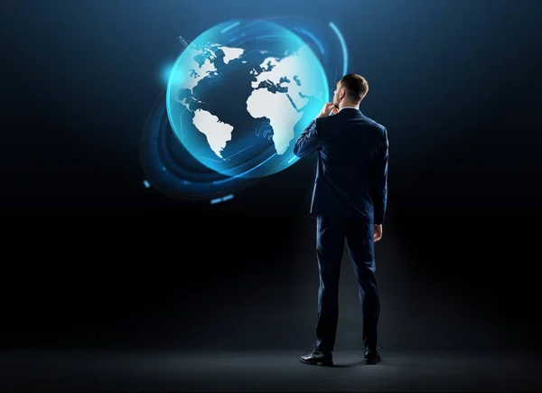 Businessman looking at earth globe hologram — Stock Photo, Image