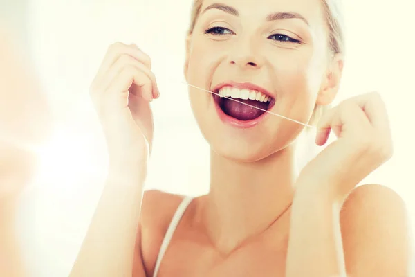 Vrouw met tandzijde reiniging van de tanden in de badkamer — Stockfoto