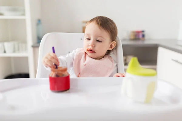 Niña con cuchara comiendo puré de tarro en casa —  Fotos de Stock