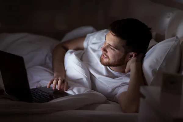 Felice giovane uomo con computer portatile a letto a casa — Foto Stock