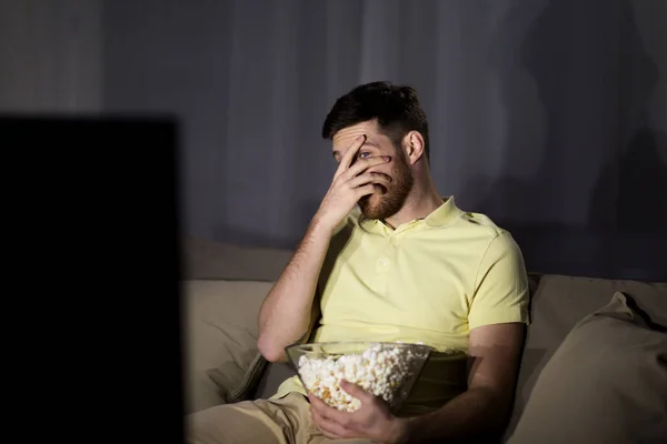 Испуганный человек смотрит телевизор и ест попкорн ночью — стоковое фото