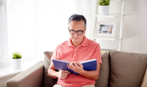 Człowiek siedzi na kanapie i czytanie książki w domu — Zdjęcie stockowe