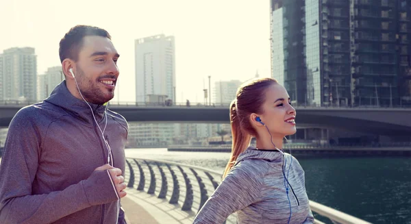 Feliz pareja con auriculares funcionando en la ciudad — Foto de Stock