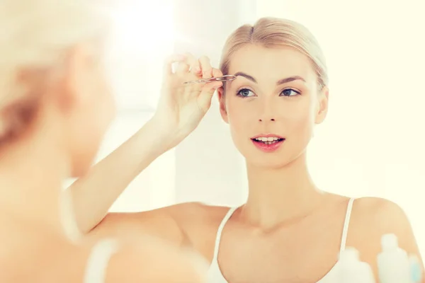 Frau mit Pinzette pinselt Augenbraue im Badezimmer — Stockfoto