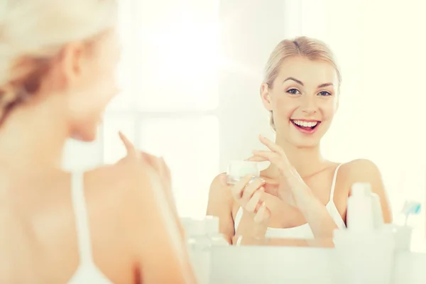 Mulher feliz aplicando creme no rosto no banheiro — Fotografia de Stock