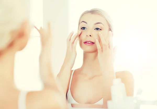 Mulher feliz aplicando creme no rosto no banheiro — Fotografia de Stock