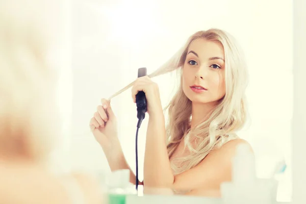 Mulher com ferro styling fazendo seu cabelo no banheiro — Fotografia de Stock