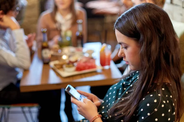 Женщина со смартфоном и друзьями в ресторане — стоковое фото