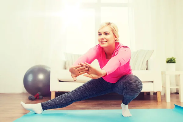 Lycklig kvinna sträcker benet på matta hemma — Stockfoto