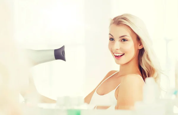 Щаслива молода жінка з вентилятором сушить волосся у ванній — стокове фото