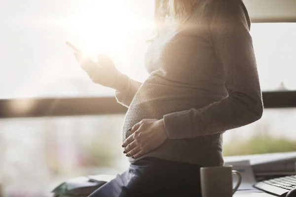 Mujer de negocios embarazada con teléfono inteligente en la oficina — Foto de Stock