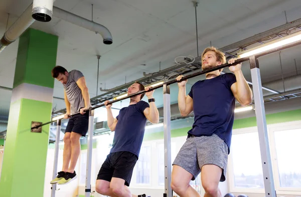 Group of young men doing pull-ups in gym — Stock Photo, Image