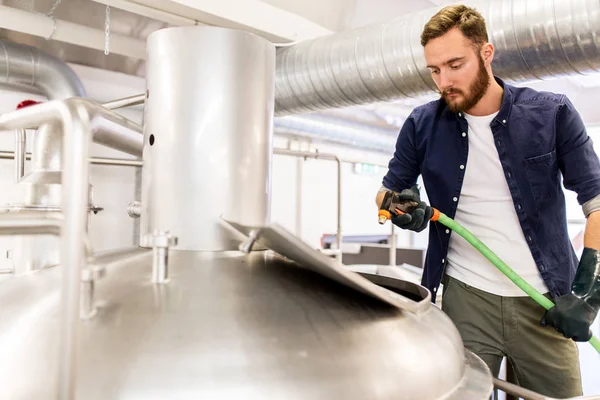 Man with hose working at craft beer brewery kettle — Stock Photo, Image